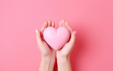 Top view female hands holding a pink heart on a pink background