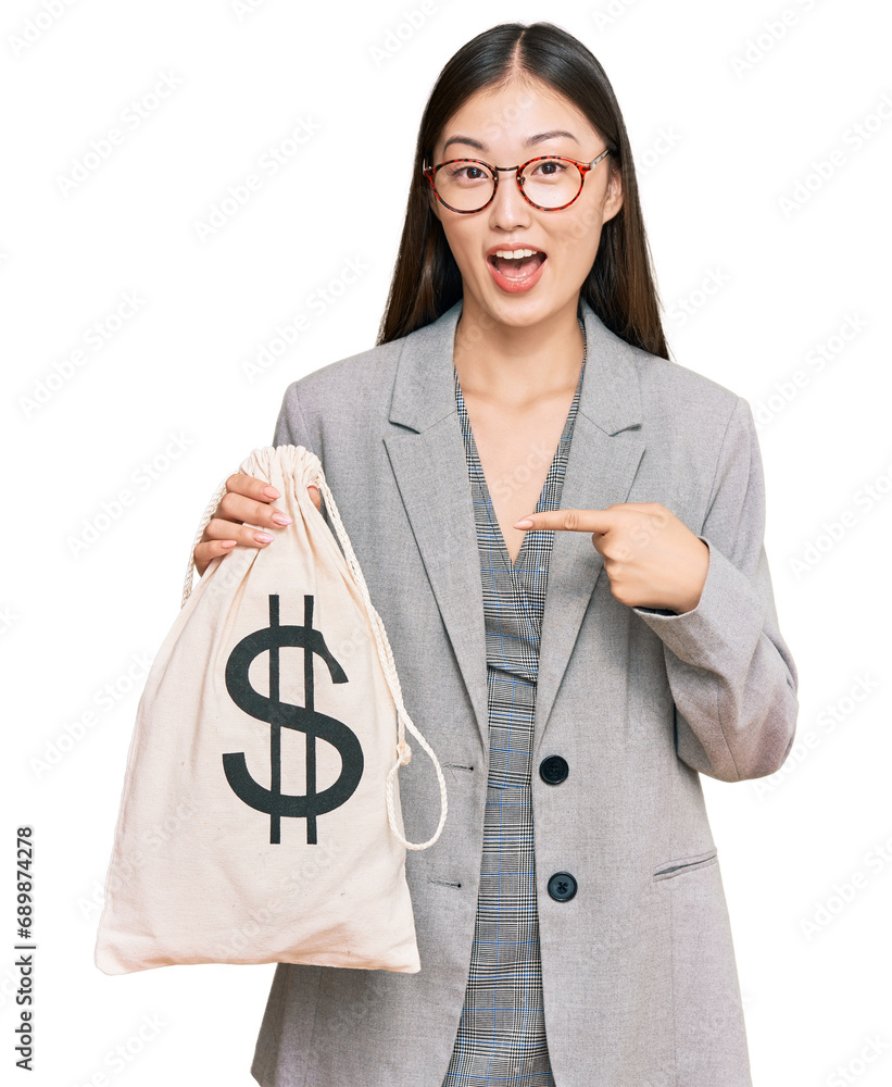 Sticker Young chinese woman wearing business suit holding dollars bag smiling happy pointing with hand and finger