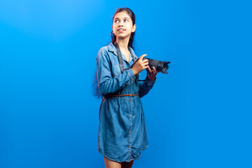 Portrait of an attractive lovely Indian girl with a digital camera looking upward against blue backdrop