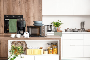 Microwave oven, coffee machine, mixer and set of plates on wooden table in modern kitchen