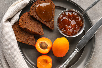 Plate with bowl of sweet apricot jam  and toasts on grey background