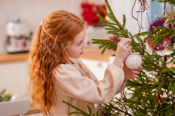 Obraz na płótnie Canvas Red-haired girl decorates the Christmas tree in a cozy homely atmosphere.