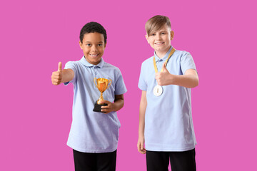 Smart little classmates in stylish uniform with prize cup and medal showing thumbs-up gesture on purple background