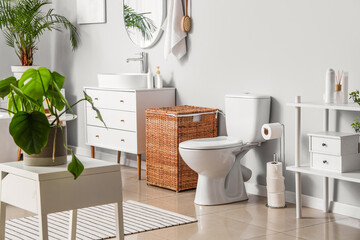 Interior of light restroom with toilet bowl and wicker basket