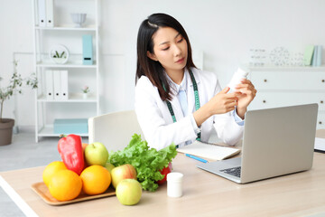 Female Asian nutritionist with pill bottle at table in office