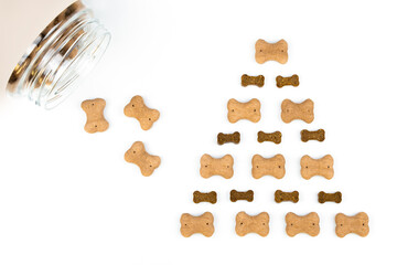 Top view of dog treats: dog biscuits and bone-shaped dog treats arranged in a pyramid shape on a white background. Dog food concept.