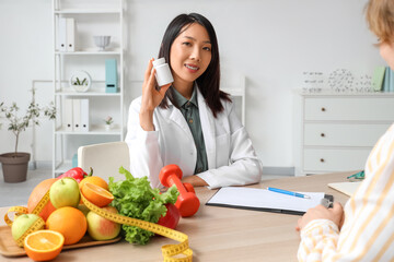 Female Asian nutritionist with pill bottle in office