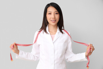 Female Asian nutritionist with tape measure on light background