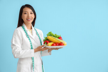 Female Asian nutritionist with vegetables on blue background