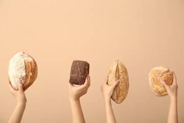 Female hands holding loaves of different fresh bread on beige background