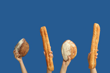Female hands holding loaves of different fresh bread on blue background