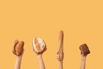 Female hands holding loaves of different fresh bread on orange background
