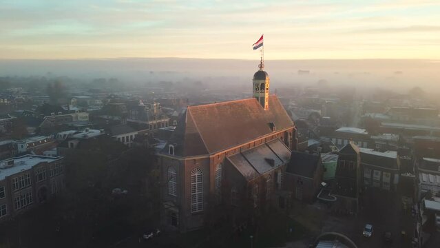 Drone view across town of Sneek with Dutch flag on top of a church at sunrise