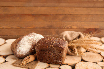Loaves of fresh bread with wheat spikelets and grains on wooden background