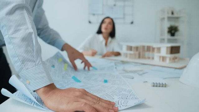 Skilled caucasian interior designer working with house model while discussing with asian architect engineer about house plan on meeting table with blueprint and house model scatter around. Immaculate.