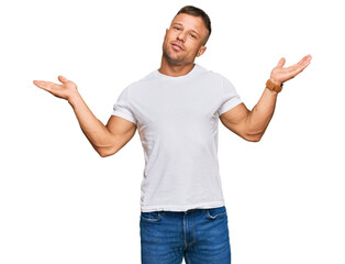 Handsome muscle man wearing casual white tshirt clueless and confused expression with arms and...