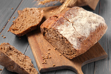 Loaf of fresh rye bread with wheat spikelets and grains on grey wooden background
