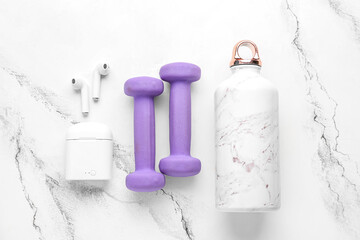Dumbbells, earphones and bottle for water on white marble background
