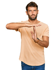 Handsome young man with beard wearing casual tshirt doing time out gesture with hands, frustrated...