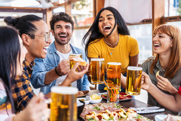 Multiethnic happy friends drinking beer glasses sitting at brewery pub restaurant table - Smiling...