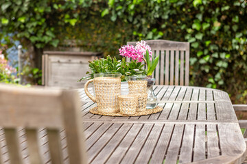 A wood table in a garden with a pot of pink flowers in California.