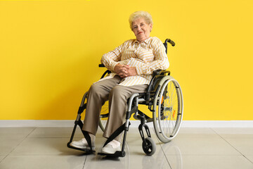 Senior woman in wheelchair near yellow wall