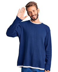 Handsome blond man with beard wearing casual sweater waiving saying hello happy and smiling, friendly welcome gesture