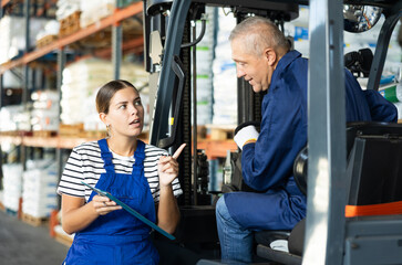 Young woman and elderly man working on loader in warehouse check documents