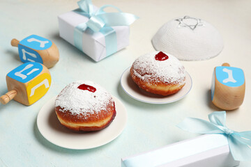 Hanukkah composition with tasty donuts, dreidels and gift boxes on light blue background