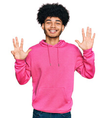 Young african american man with afro hair wearing casual pink sweatshirt showing and pointing up with fingers number nine while smiling confident and happy.