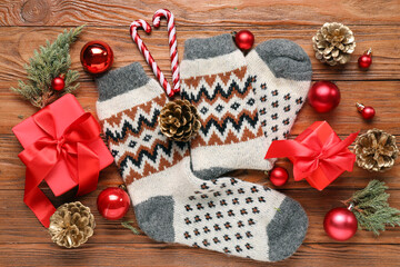 Knitted socks with Christmas decorations, fir branches and gift boxes on wooden background