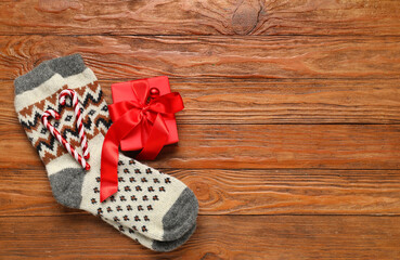 Knitted socks with Christmas gift box and candy canes on wooden background