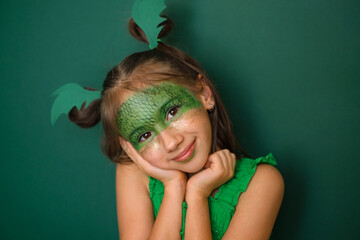 A cute beautiful girl with makeup with a painted dragon and gold sequins on her cheeks. A headdress...
