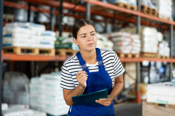 Fototapeta premium Young woman warehouse worker in uniform check documents in warehouse