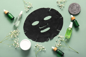 Facial sheet mask with different cosmetic products and gypsophila flowers on green background