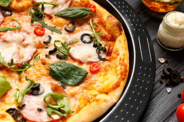 Pizza with ham on a black baking dish on a dark wooden background, top view.