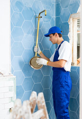 Focused young plumber in blue overalls working in apartment under renovation, installing shower in...