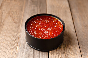 Red salmon caviar in a black tin can on wooden background.