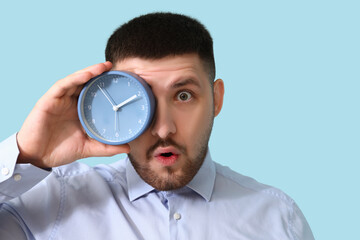Young shocked businessman with alarm clock showing OK gesture on blue background. Time management...