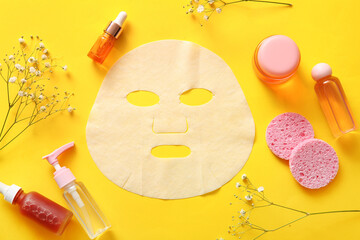 Facial sheet mask with different cosmetic products and gypsophila flowers on yellow background