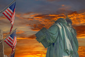 Statue of Liberty is framed by beautifully waving American flag during sunset