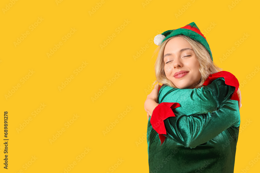 Sticker Beautiful young woman dressed as elf hugging herself on yellow background