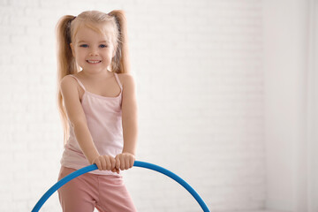 Cute little girl with hula hoop doing gymnastics in gym