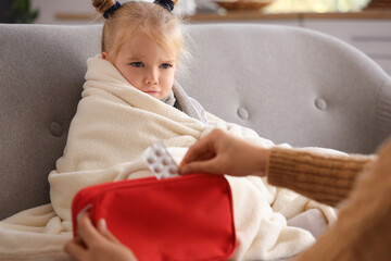 Sick little girl and her mother with first aid kit at home
