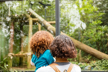 Black mother and white Caucasian daughter watching birds on a walk in the zoo