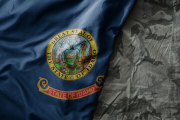 waving flag of idaho state on the old khaki texture background. military concept.