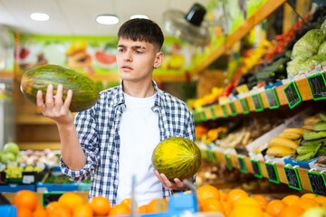 Interested man visiting greengrocery store, choosing ripe sweet melon from counter