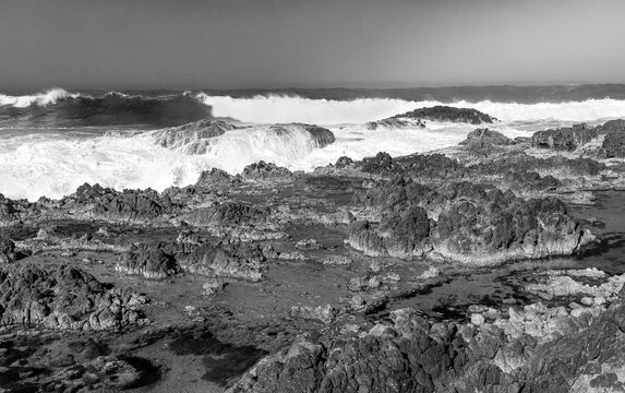 Classic black and white rocky Pacific Ocean shore with crashing waves on the central coast of Oregon.