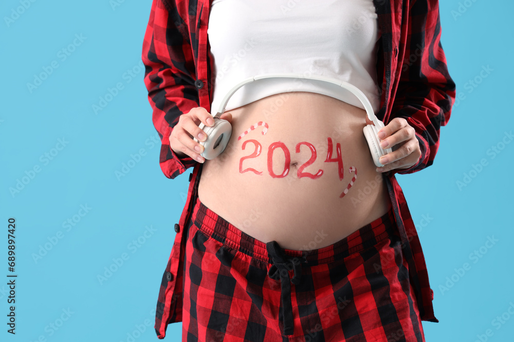 Canvas Prints beautiful young pregnant woman with headphones and drawn 2024 year on her belly against blue backgro