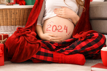 Beautiful young pregnant woman with drawn 2024 year on her belly sitting in room, closeup